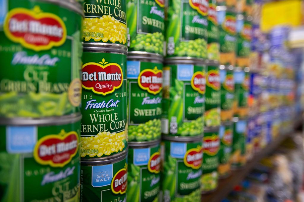 Estantería de supermercado con múltiples latas de conservas vegetales Del Monte, destacando la marca y el etiquetado de productos como maíz dulce y guisantes.